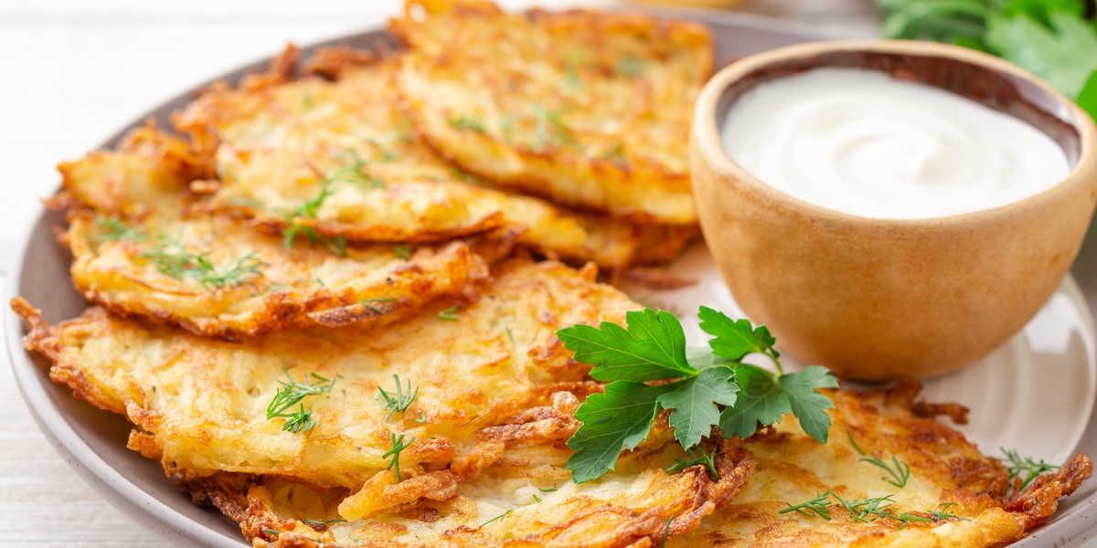 Potato pancakes or latkes or draniki with sour cream in plate on white wooden table