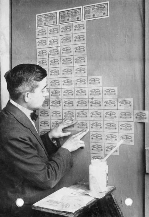 Mężczyzna tapetujący ścianę bezwartościowymi banknotami w czasie hiperinflacji w Republice Weimarskiej