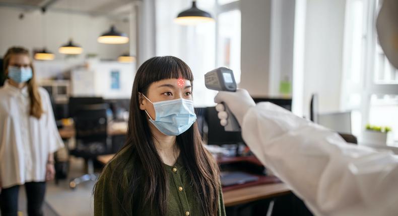 Woman wearing protective mask goes through a temperature checks before going to work in the office.
