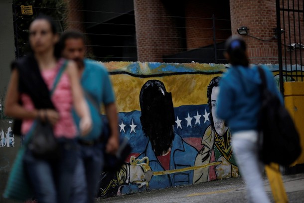 Venezuelan citizens walk past a mural depicting former Venezuela's late President Hugo Chavez in Car