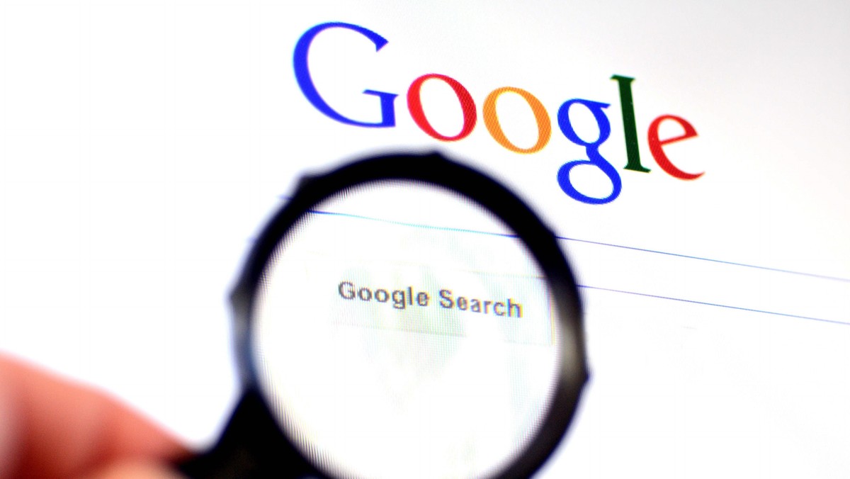 Hand holds Magnifying glass against Google homepage