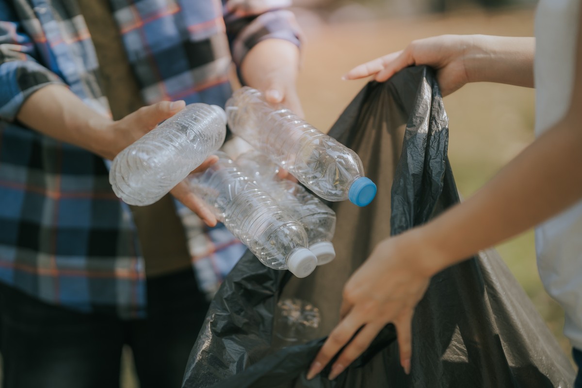Mężczyzna wyrzuca do worka butelki plastikowe, segregując śmieci