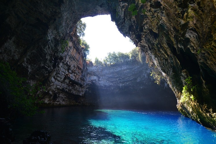 <strong>Kefalonia, Jaskinia Melissani</strong>
<br></br>
Wyprawa do jaskini Melissani to jak przekraczanie granicy do innego świata – świata nimf, które według mitologii, są powiązane z tym miejscem. Prowadzi do niego szerokie, nieco poszarpane wejście. Gdy pokonamy już korytarze tuneli, naszym oczom ukarze się serce jaskini – olbrzymia przestrzeń zalana tak krystalicznie czystą wodą, że można policzyć kamienie znajdujące się na dnie, choć głębokość wynosi tu kilkanaście metrów! Światło słoneczne wpada tutaj przez naturalny otwór w sklepieniu, który powstał tysiące lat temu w skutek zapadnięcia się górnej warstwy. Dzięki temu można podziwiać magiczne kolorowe refleksy rozświetlające to podziemne jezioro. 
<br></br>
Miejsce to zostało odkryte w 1951 roku przez Greka, Gianniego Petrochelios’a. Przez kolejne lata dostęp do niego mieli wyłącznie badacze, którzy w trakcie swoich prac odkryli wiele ciekawych przedmiotów, w tym antyczne lampy oliwne i relikty świadczące o tym, że jaskinia była niegdyś ważnym ośrodkiem kultu. Wszystko wskazuje na to, że oddawano tutaj hołd Nimfom, przez co często określa się to miejsce jako „jaskinia nimf”. Jej nazwa pochodzi od imienia jednej z nich – Mellisanthi, która zgodnie z legendą, utopiła się, gdy jej ukochany bożek Pan, nie odwzajemnił jej uczucia.   
<br></br>
Dziś ten mały raj ukryty pod powierzchnią Kefalonii dostępny jest dla wszystkich i warto to wykorzystać – tym bardziej, że łatwo dostać się tu promem z pobliskiej Zakhyntos. Możliwość odwiedzenia tego miejsca to niezapomniane doświadczenie.
<br></br>
<a  href=