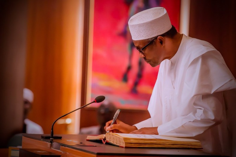 President Buhari affixes his signature on a document (Presidency) 