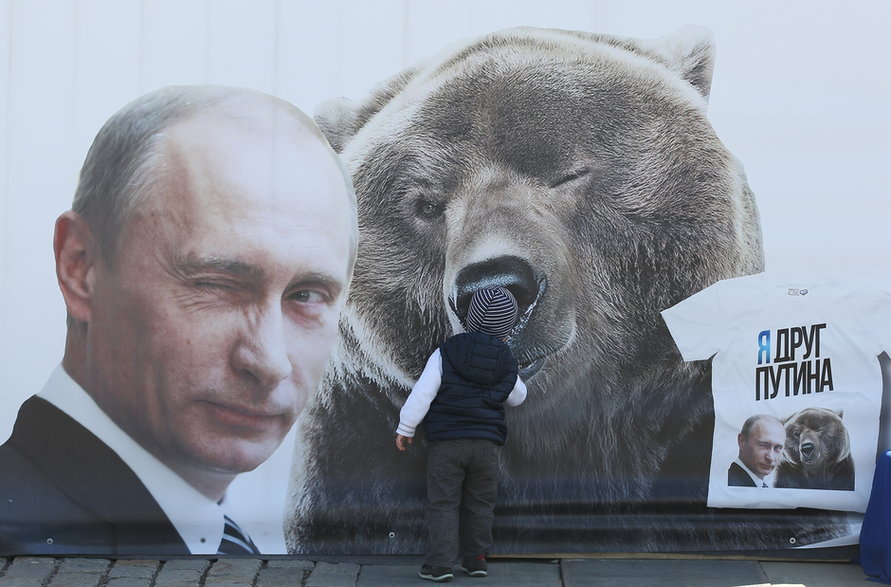 Chłopiec oglądający billboard przedstawiający mrugającego prezydenta Rosji Władimira Putina i niedźwiedzia oraz koszulkę z napisem: "jestem przyjacielem Putina", Moskwa, 8 maja 2015 r.