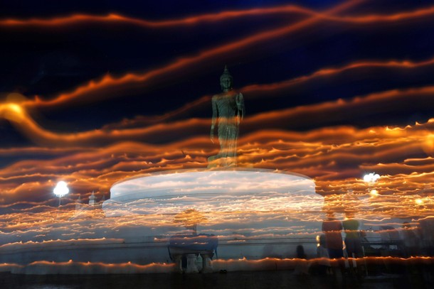 Buddhists carry candles while encircling a large Buddha statue during Asanha Puja Day, the eve of th