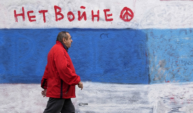Mężczyzna przechodzący obok ściany, na której kiedyś widniał mural rosyjskiego prezydenta Władimira Putina. Został zamalowany biało-niebieską flagą na znak sprzeciwu wobec rosyjskiej inwazji na Ukrainę, Belgrad, 6 grudnia 2022 r.