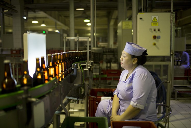 Ułan Bator, Mongolia. Pracownica fabryki APU JSC obserwuje butelki piwa Niislel przesuwające się po taśmie produkcyjnej i sprawdza, czy żadna z nich nie ma defektów. Koncern APU to największy producent napojów alkoholowych w Mongolii.