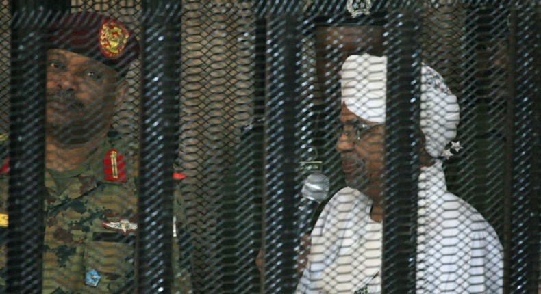 Sudan's deposed military ruler Omar al-Bashir stands in a defendant's cage at the opening of his corruption trial in Khartoum in August