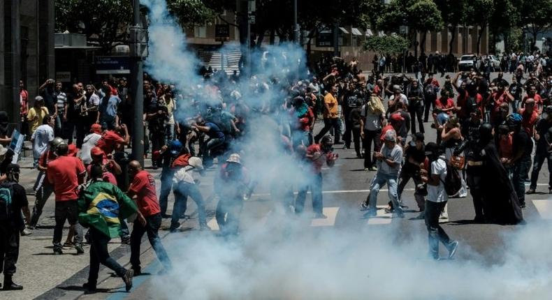 Protesters run away from tear gas during clashes with riot police following a public servants protest against austerity measures in front of the Rio de Janeiro state assembly on December 6, 2016