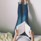 Woman Lying On Bed Reading Book With Legs Raised