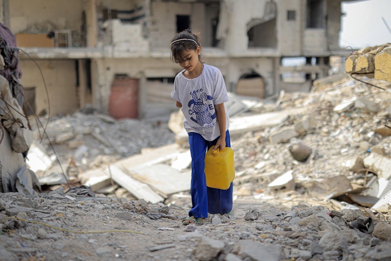 Dana Hussam Ziyad, 10-letnia dziewczynka mieszkająca z ojcem w zniszczonym budynku w dzielnicy Nasr na zachód od miasta Gaza. Dana straciła prawą rękę, trójkę rodzeństwa i kilku innych członków rodziny w izraelskim ataku. Dziewczynka niesie wodę, 2 lipca 2025 r.