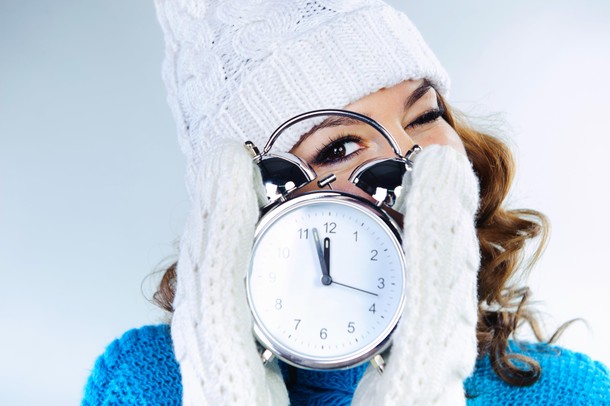 Beautiful young girl in winter clothes with alarm clock