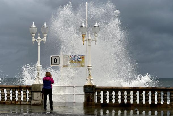 A woman takes pictures as a huge wave crashes against the promenade at San Lorenzo beach in Gijon
