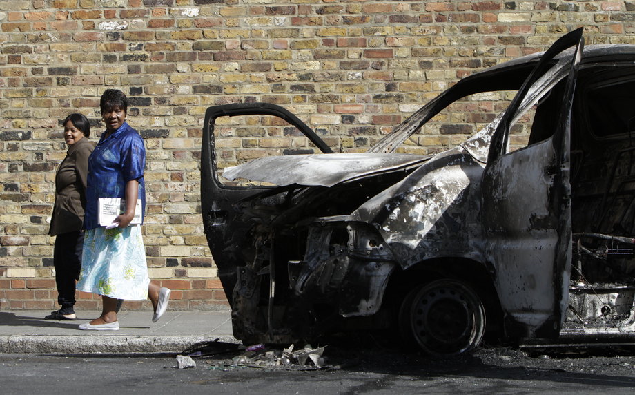 Two women passing a burned-out van on August 9, 2011, after riots and looting in Hackney.