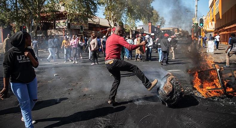 A man kicks a burning piece of furniture during a riot in the Johannesburg suburb of Turffontein on September 2, 2019 [Michele Spatari/AFP]