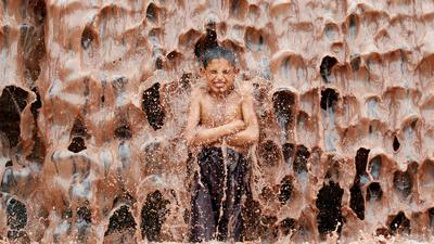 An Afghan boy cools off under a muddy waterfall on the outskirts of Jalalabad province