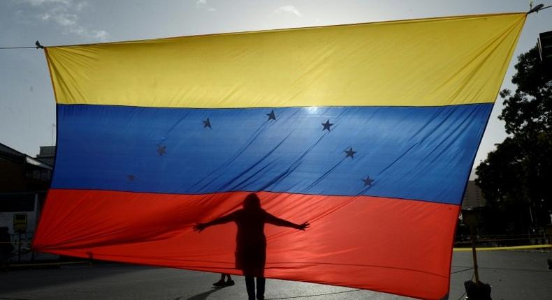 A protester's shadow is cast on a Venezuelan national flag in Caracas, the capital city of a country that has hit its 100th day of anti-government protests