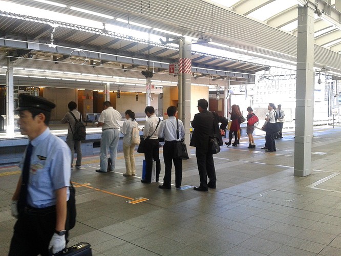 Również pasażerowie spokojnie oczekują na przyjazd pociągu, ustawiając się w kolejce wzdłuż wyznaczonej linii.