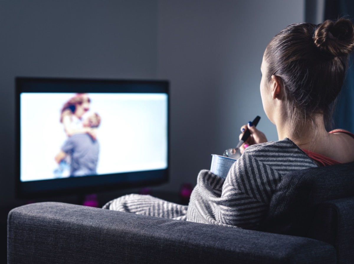 Kobieta ogląda telewizję i je lody.
