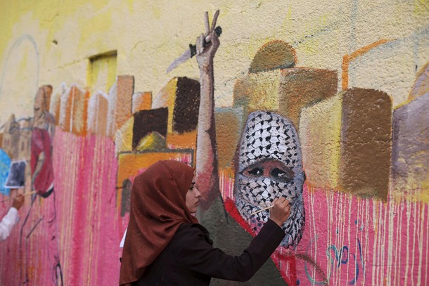 Palestinian woman paints a mural, depicting a masked Palestinian holding a knife, in support of Pale