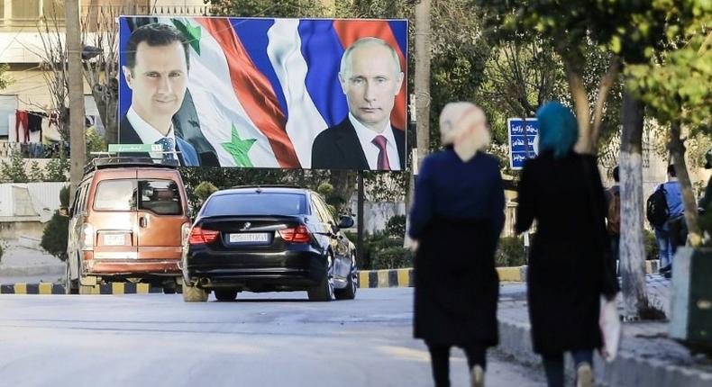 Syrians walk past a giant poster of President Bashar al-Assad and his Russian counterpart Vladimir Putin in the northern Syrian city of Aleppo