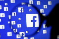 A man poses with a magnifier in front of a Facebook logo on display in this illustration taken in Sa