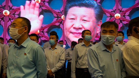 Zwiedzający stoją wewnątrz Miejsca Pamięci Pierwszego Krajowego Zjazdu Komunistycznej Partii Chin, podczas gdy z tyłu na ekranie widać prezydenta Chin Xi Jinpinga