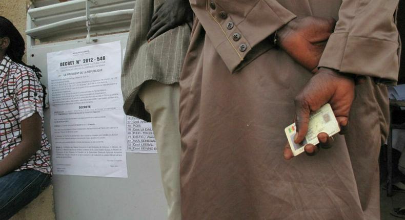 Sénégal : un homme tenant une ancienne carte d'électeur devant un bureau de vote