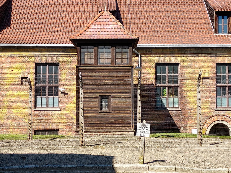 Auschwitz I, za drutami okalającymi obóz widoczny budynek przyjęć do obozu.