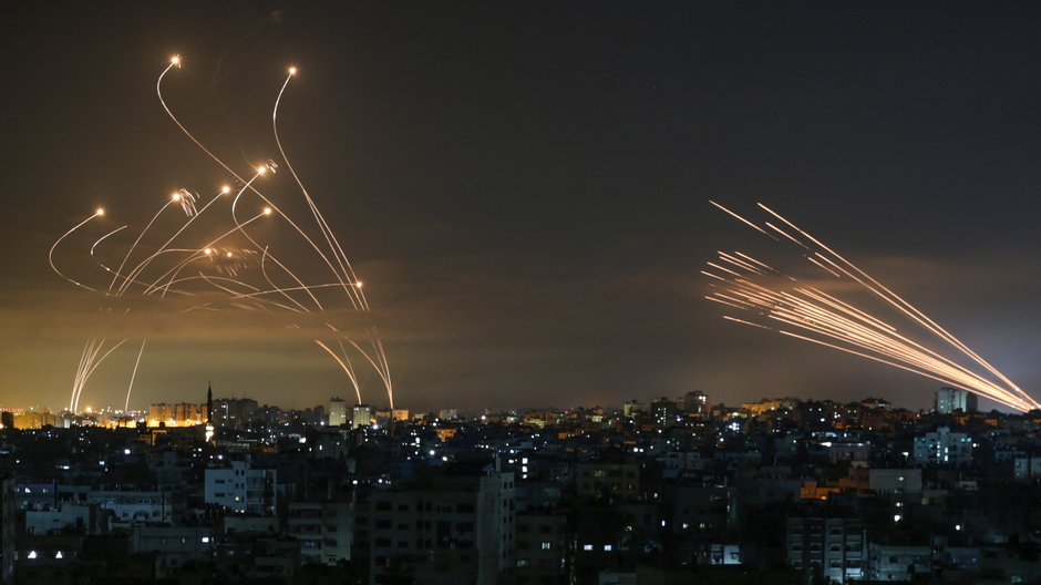 Izraelski system obrony przeciwrakietowej Iron Dome (L) przechwytuje rakiety (R) wystrzelone przez ruch Hamasu w kierunku południowego Izraela z Beit Lahia w północnej Strefie Gazy, widziane na niebie nad Strefą Gazy w nocy 14 maja 2021 r.