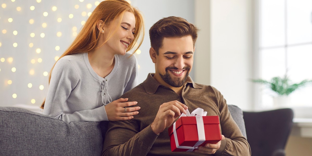 Young happy man boyfriend opening present box from his loving smiling girlfriend