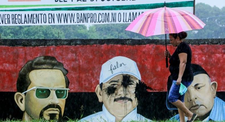 A woman passes by a graffiti depicting leaders of the revolution, including incumbent President Daniel Ortega (C), in San Jorge