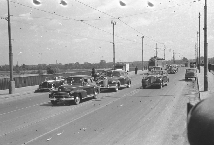 Chevrolet model z 1946 roku (wóz ochrony) prowadzi kolumnę samochodów rządowych. Z tyłu obok i za tramwajem widocznych co najmniej 6 kolejnych Chevroletów