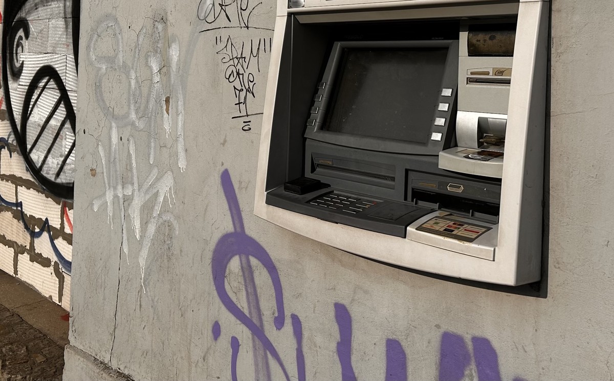 Bankomat wbudowany w ścianę budynku pokrytą licznymi graffiti, w tym dużym fioletowym symbolem dolara. Niebawem gotówkę będzie można pobierać bez karty
