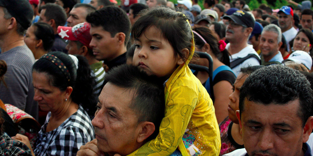 A man carries a child as people line up to cross over the Simon Bolivar international bridge to Colombia to take advantage of the temporary border opening in San Antonio del Tachira, Venezuela, July 17, 2016.