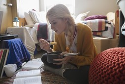 Female college student eating and studying on floor in dorm room