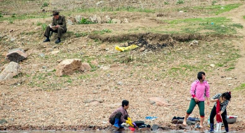 A North Korean soldier reads a book near women washing clothes in the Yalu border river on April 16, 2017