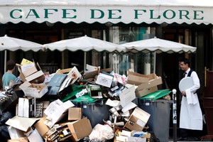 A waiter stands near a pile of rubbish bags in front of the Cafe de Flore in Paris during a strike of garbage collectors and sewer workers of the city of Paris to protest the labour reforms law proposal