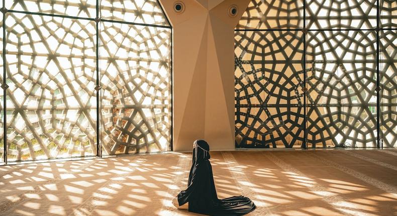 Woman praying in a mosque with openwork windows {image Credit: Hatice Baran]