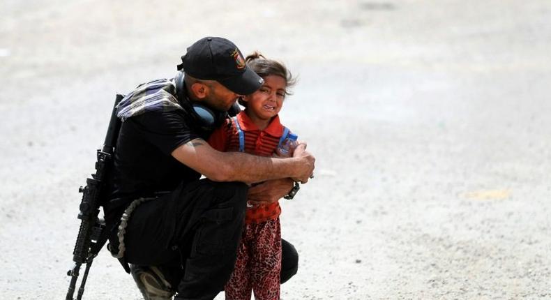 An Iraqi soldier helps a girl whose family has fled their home in the west of Mosul on May 26, 2017