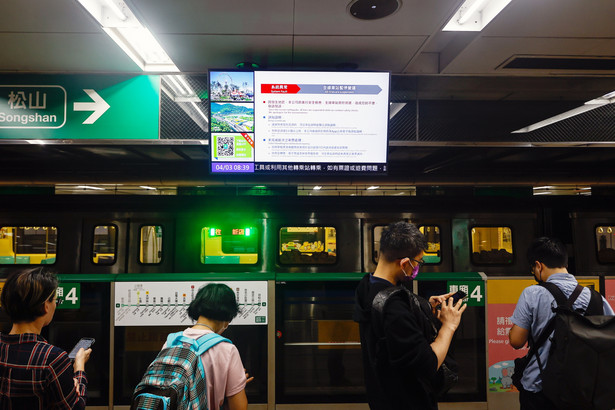Pasażerowie czekają pod ekranem emitującym ogłoszenie o zawieszeniu pociągu metra po trzęsieniu ziemi