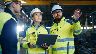 Male and Female Industrial Engineers Talk with Factory Worker while Using Laptop. They Work at the Heavy Industry Manufacturing Facility.