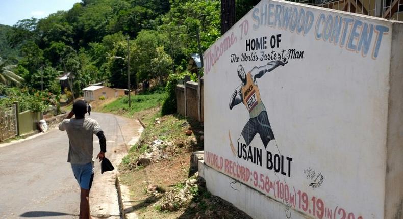 A boy walks past a welcome sign depicting Jamaican sprinter Usain Bolt at an intersection in his hometown of Sherwood Content, Jamaica