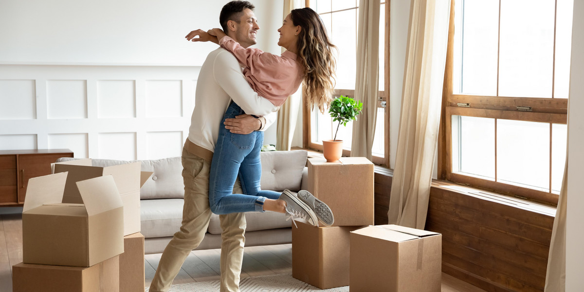 Happy husband lifting excited wife celebrating moving day with boxes