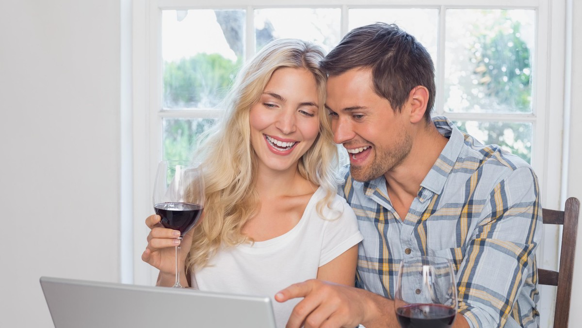 Couple with wine glasses using laptop at home