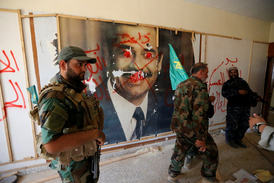 Fighters from the Iraqi Shi'ite Badr Organization walk past a poster depicting images of former Iraqi President Saddam Hussein on the outskirts of Fallujah.