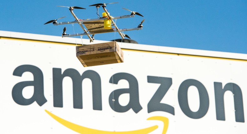 An early version of an Amazon drone flies in front of the company logo.