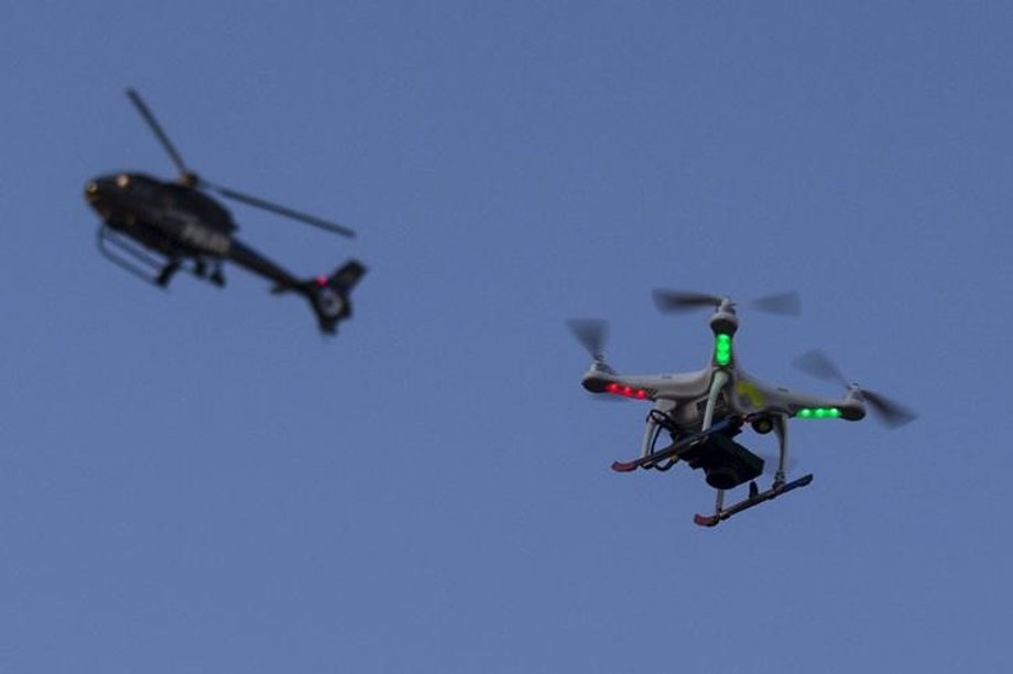 A police helicopter flies past a UAV drone Quadcopter over west Baltimore, Maryland, May 2, 2015.