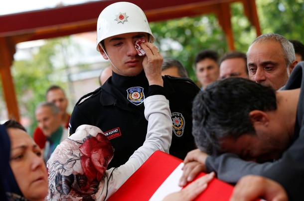 A woman wipes the tears of an honour guard as he stands next to the coffin of police officer Karagoz